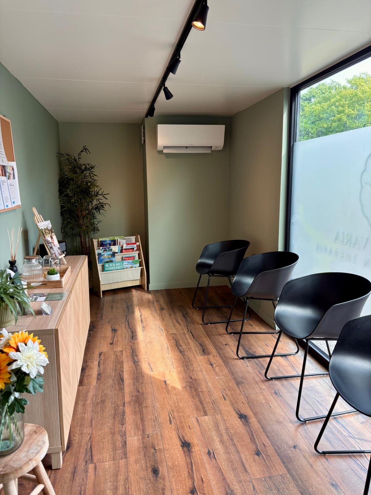 Inkijk in de wachtruimte met stoelen en houtvloer