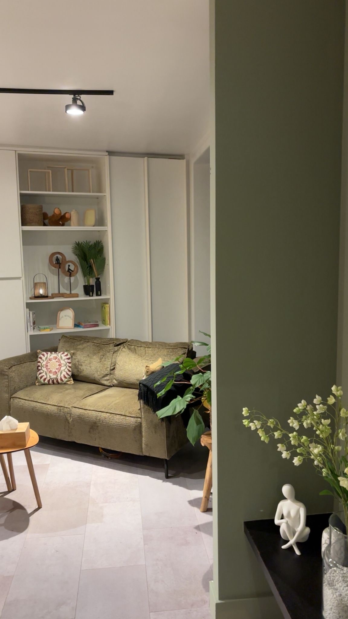 Doorkijk naar zithoek met sofa, bloemen en groene wand